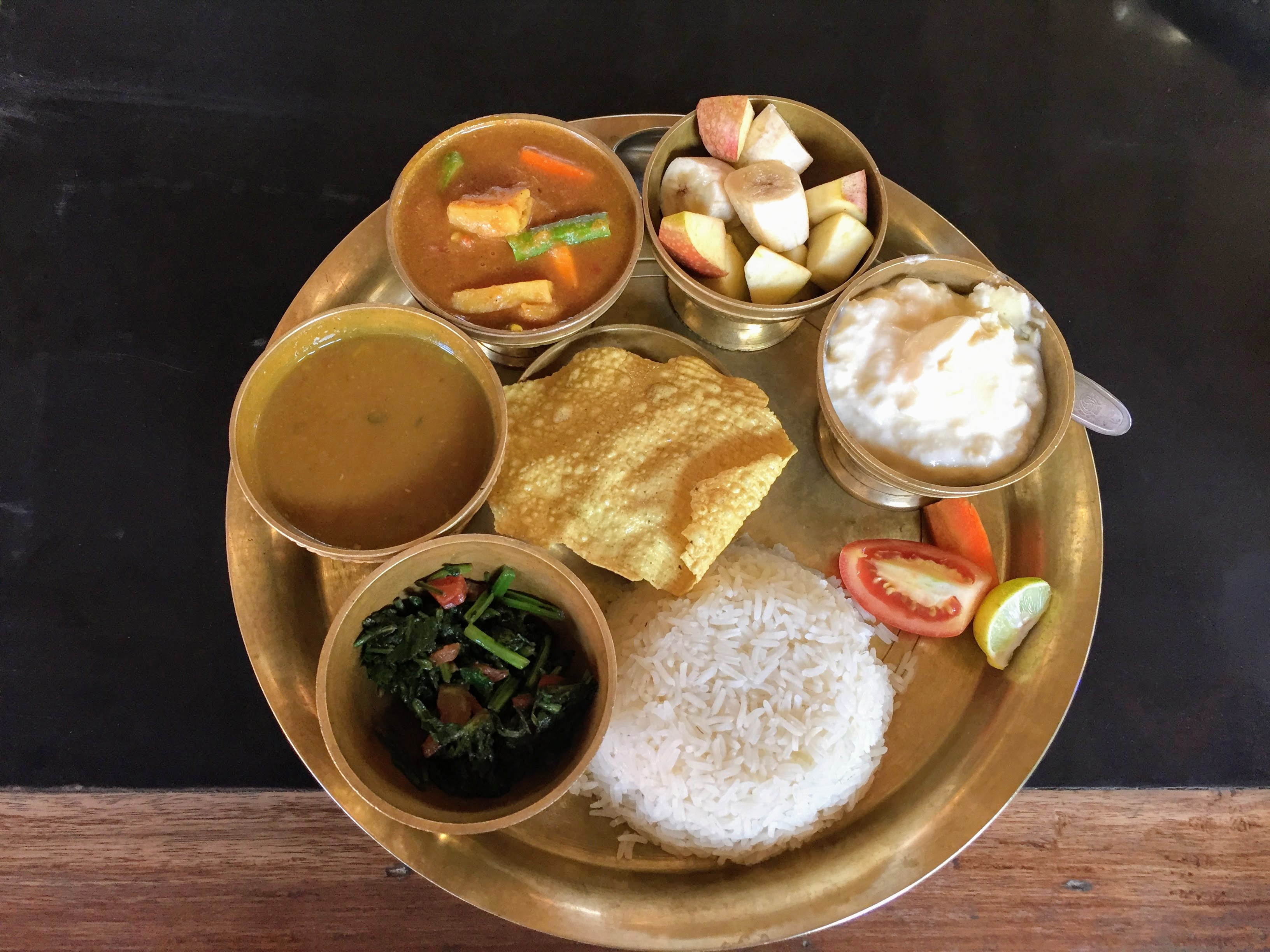 Sebuah thali dal-bhat dengan nasi putih, sup lentil, sayuran hijau goreng, kari sayuran, yogurt, papad, dan salad sayuran.