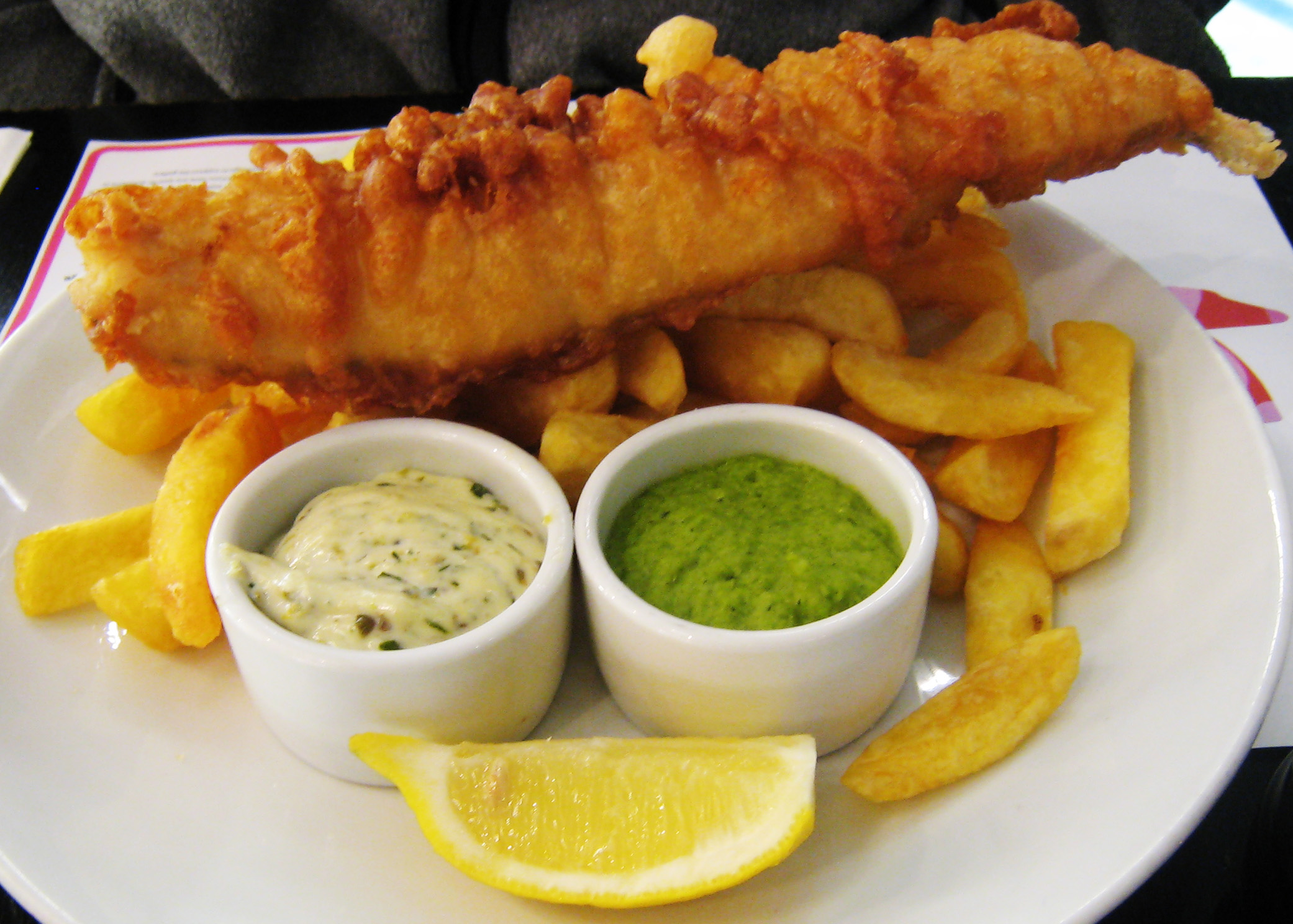 Ikan dan kentang goreng, hidangan tradisional British, dihidangkan dengan lemon, sos tartar dan kacang polong lumat