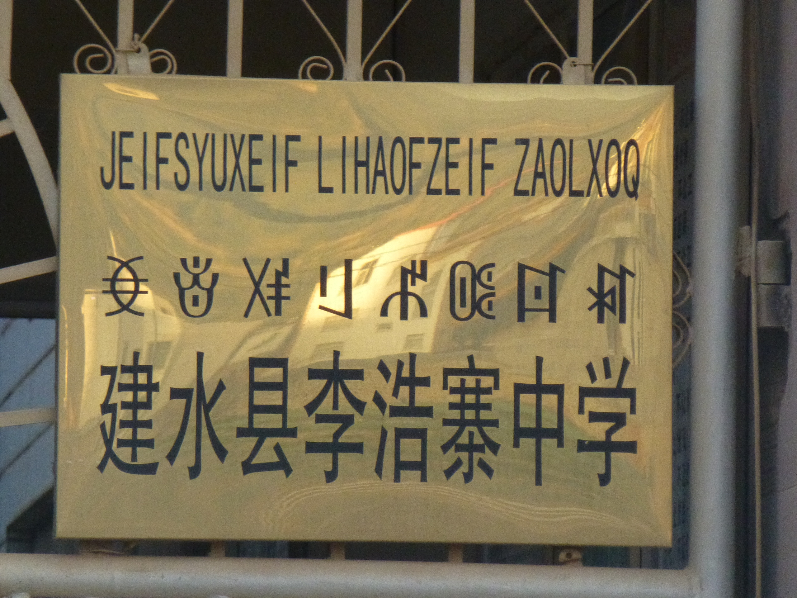 Sebuah tanda di sebuah sekolah menengah di Jianshui, Yunnan, ditulis dalam Hani menggunakan aksara Latin, Nisu menggunakan aksara Yi, dan bahasa Tionghoa.
