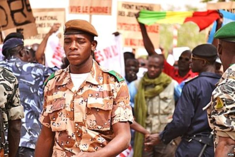Seorang prajurit Garda Nasional berjalan melewati para demonstran di Bandara Bamako.