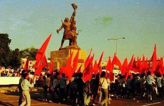 Orang ramai meraikan kemenangan Revolusi 14 Oktober di Yaman Demokratik dengan mengibarkan bendera merah di sebelah Patung Kebebasan